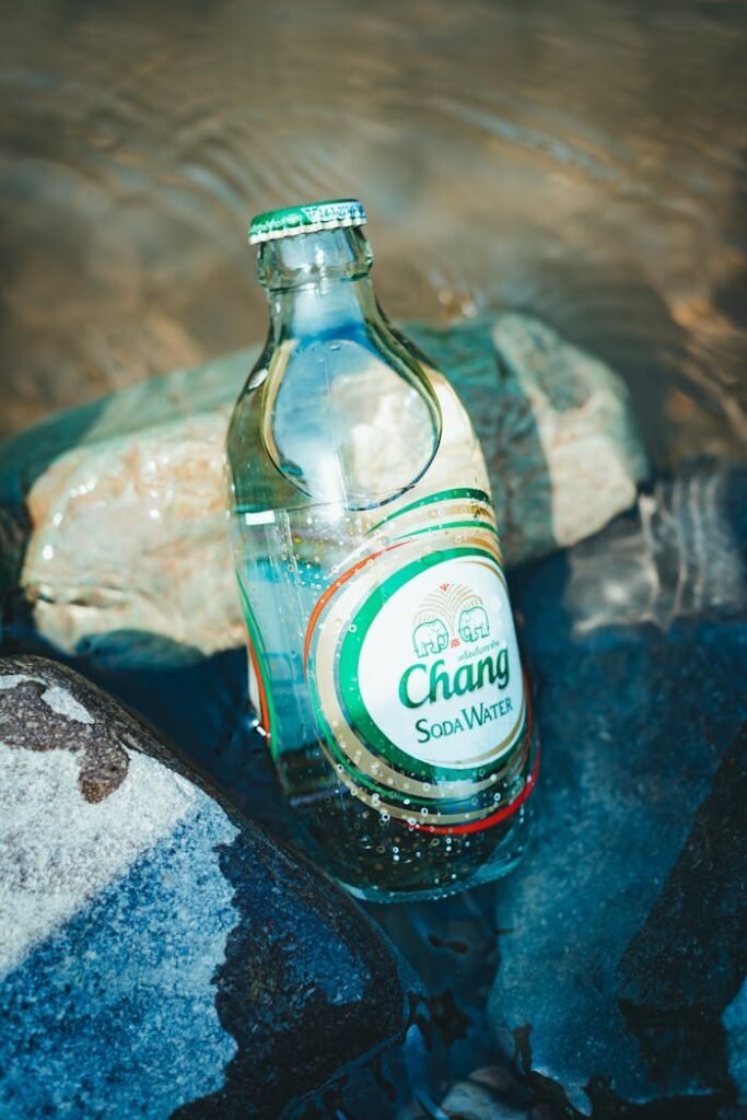 A glass soda water bottle partially submerged among rocks in clear water.